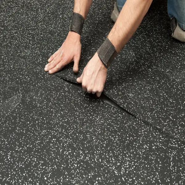 Installing black Gym rubber flooring with a scraper.