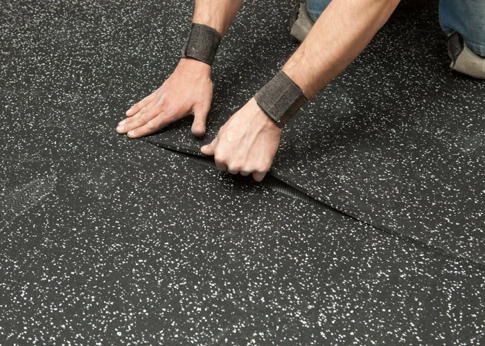 Hands installing speckled black rubber flooring on a floor